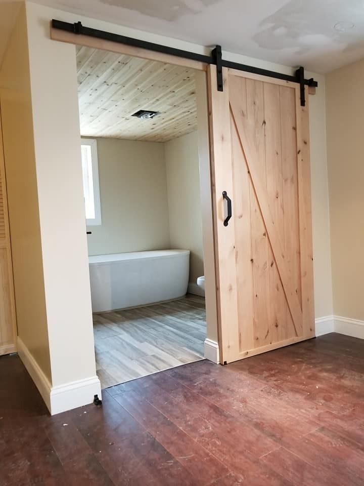 Barn door, light wood, with black hardware, leading to a bathroom with a white bathtub.