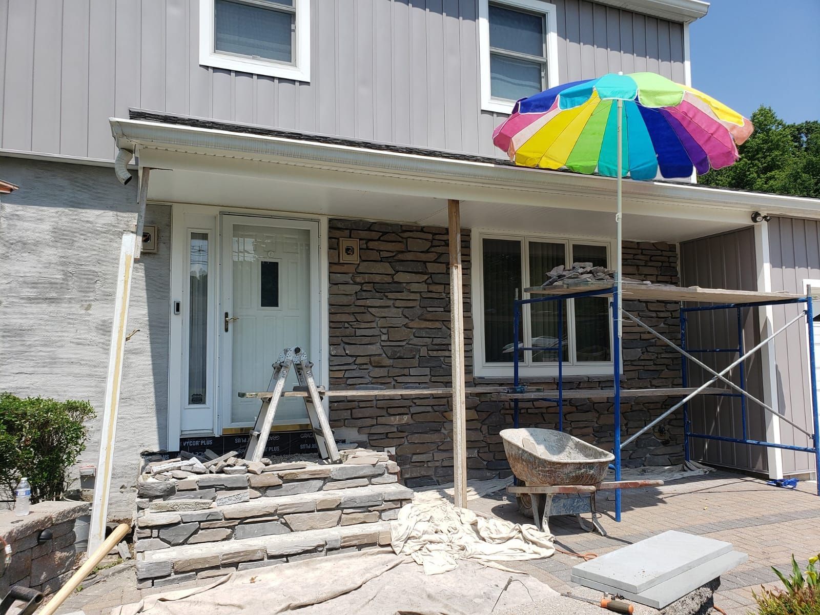 House exterior renovation: stone facade installation, scaffolding, and colorful umbrella.