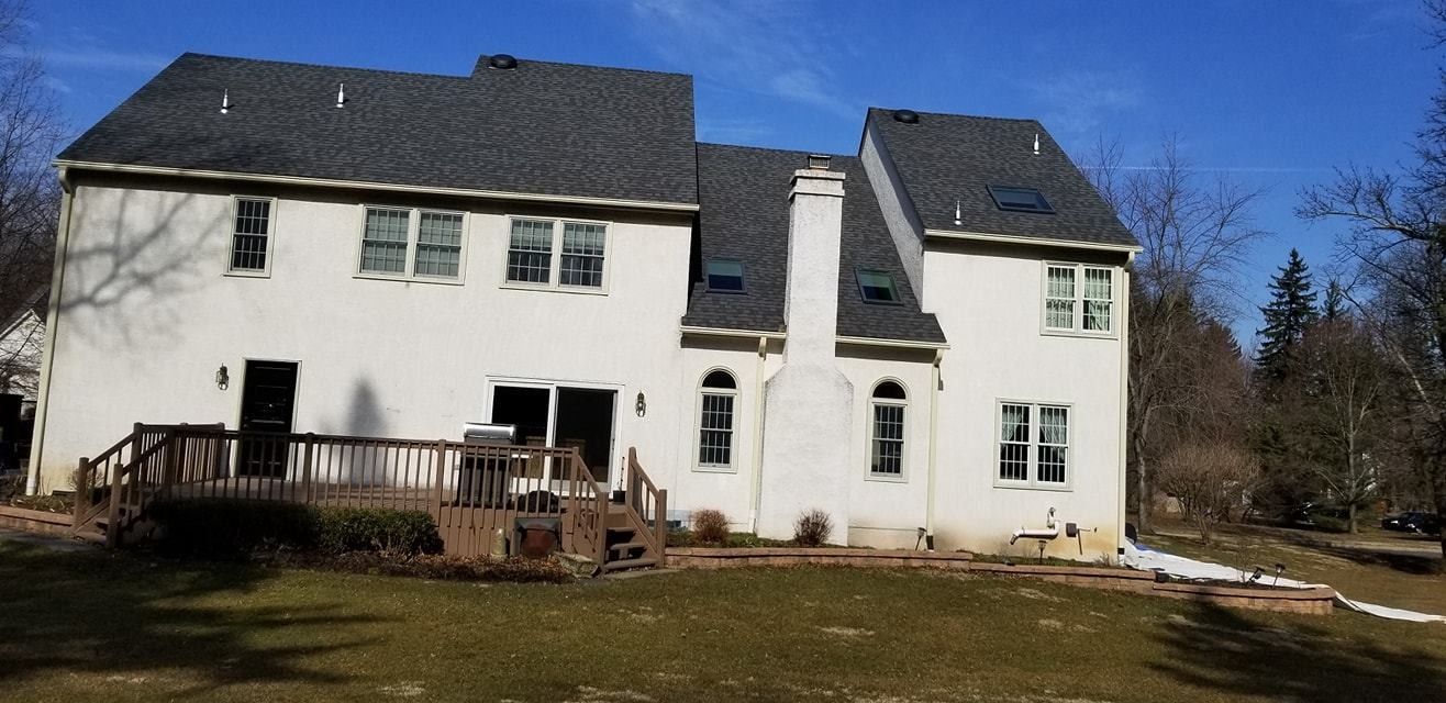 White house with dark gray roof, deck, and green lawn against a blue sky.