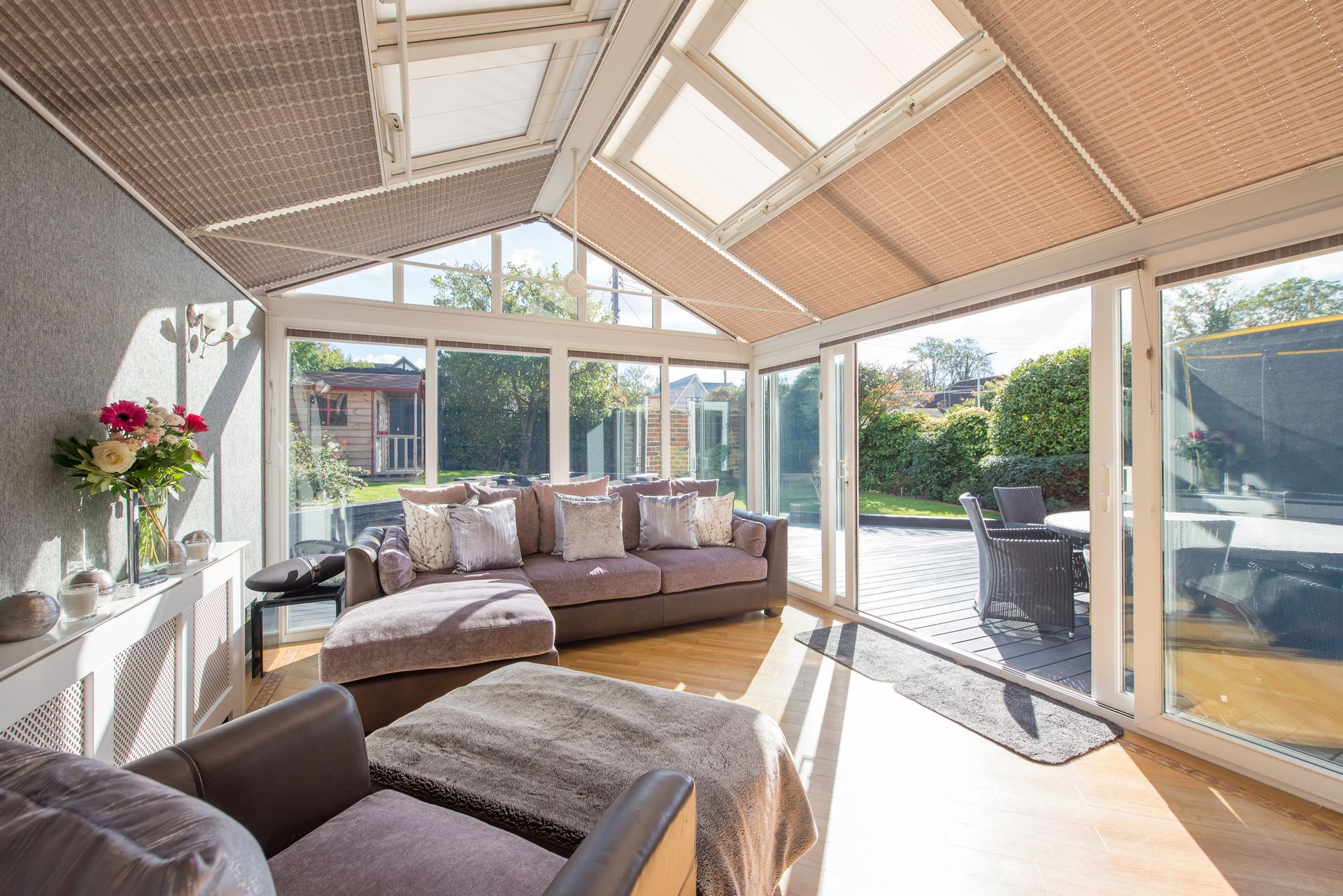 Sunroom interior with glass walls, brown sofa, skylights, and a view of a patio and garden.
