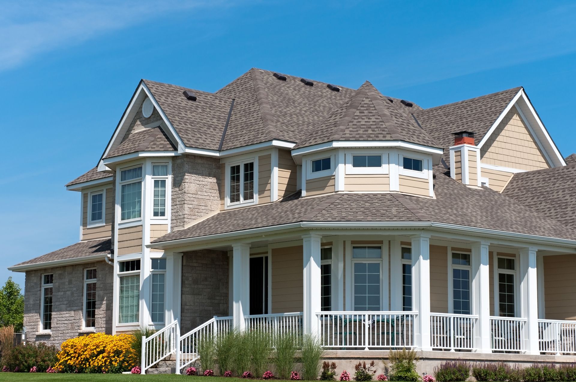 Two-story house with gray roof, beige siding, white trim, porch, and blue sky.