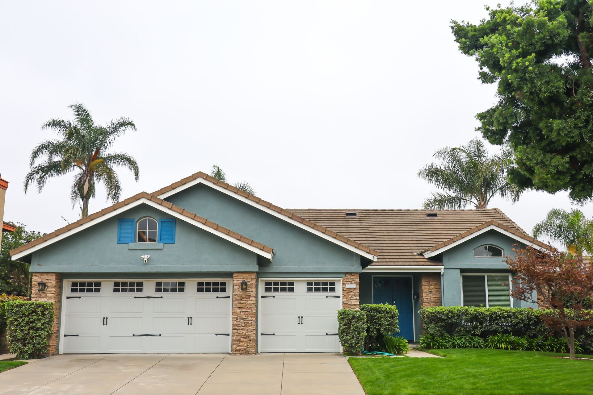 Blue house with two-car garage, stone accents, and green lawn under a cloudy sky.