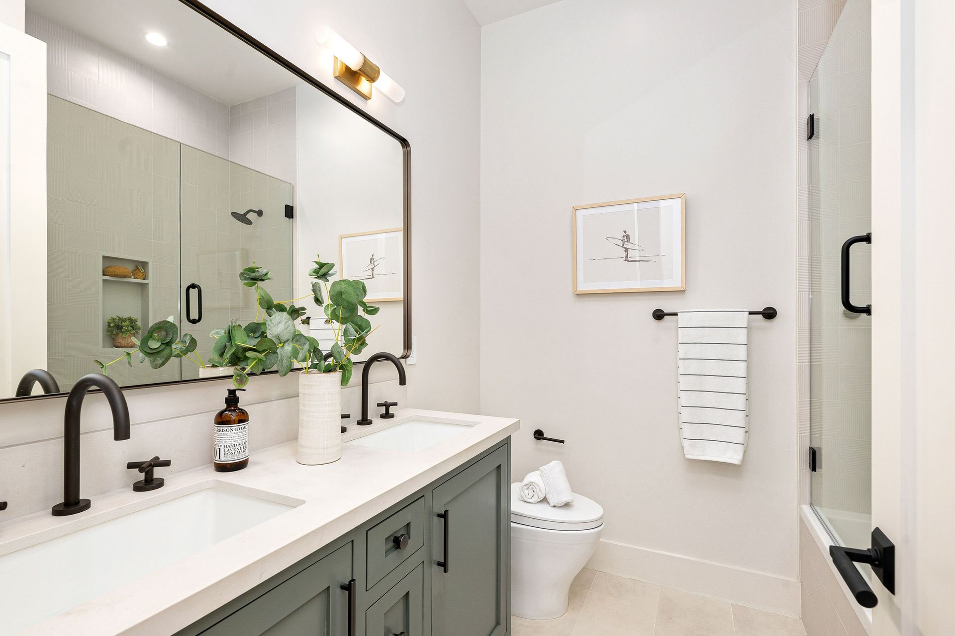 Bathroom with gray vanity, black fixtures, large mirror, white walls, and a small framed print.