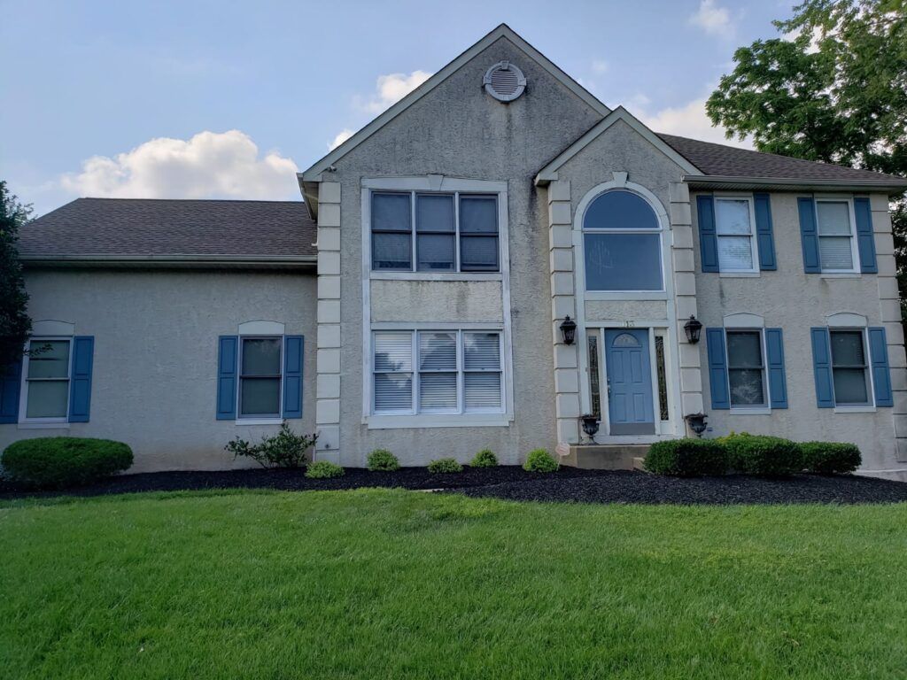 Two-story house with stucco exterior, blue shutters, and green lawn.
