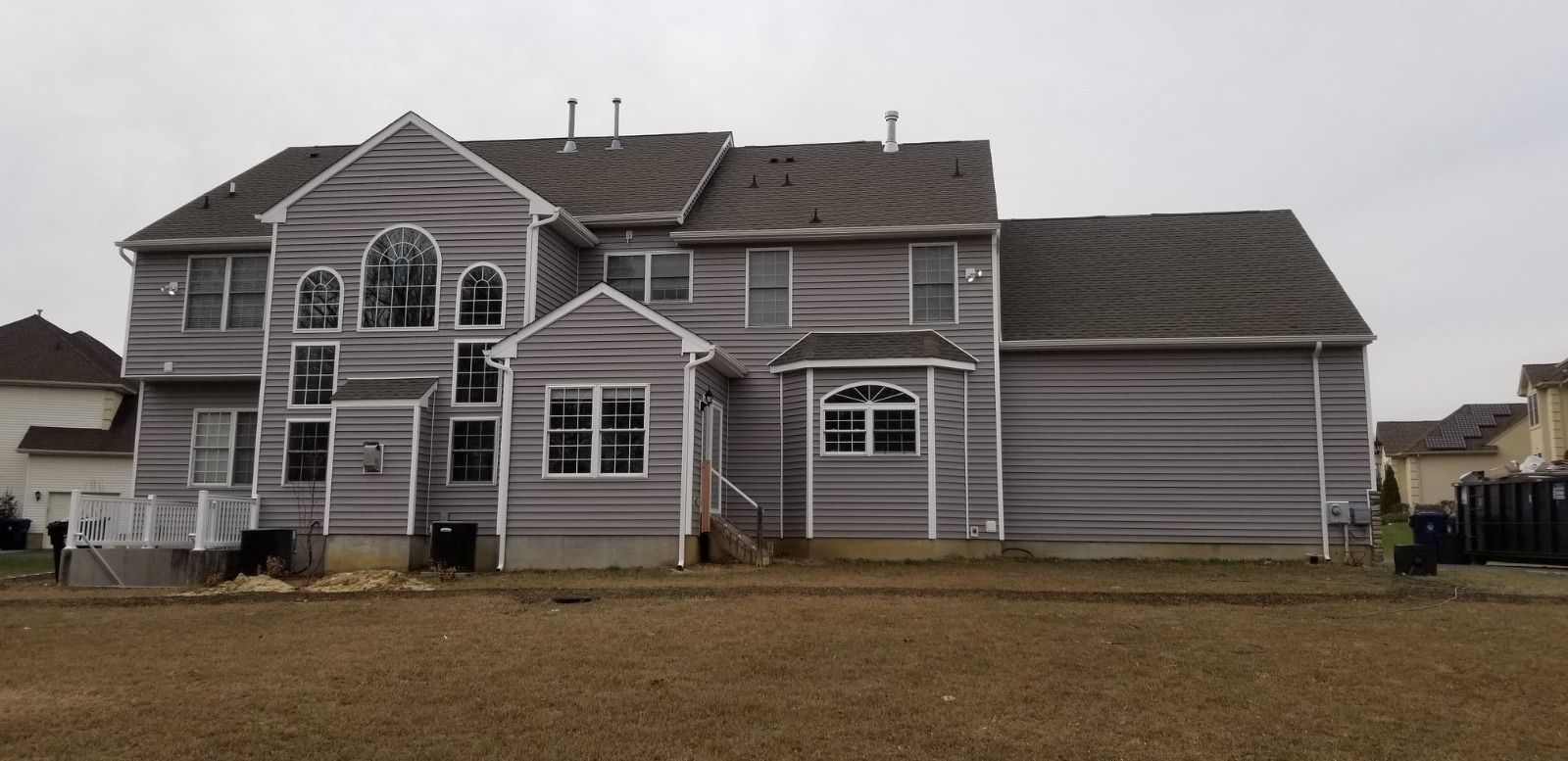 Back view of a large, two-story house with gray siding and roof on a cloudy day.