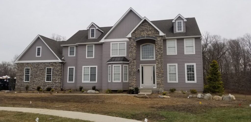 Large gray house with stone accents and a white front door, surrounded by a brown yard.