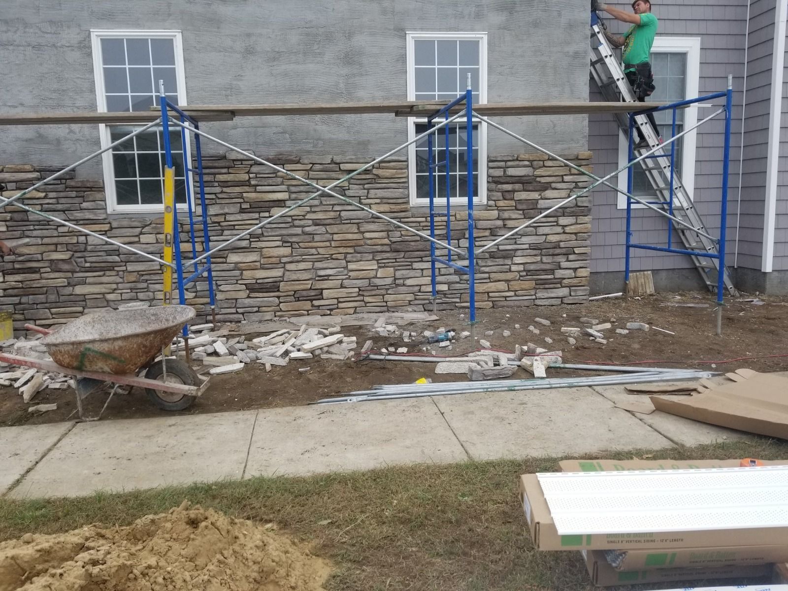 Construction worker on scaffolding, installing stone facade on a house exterior.