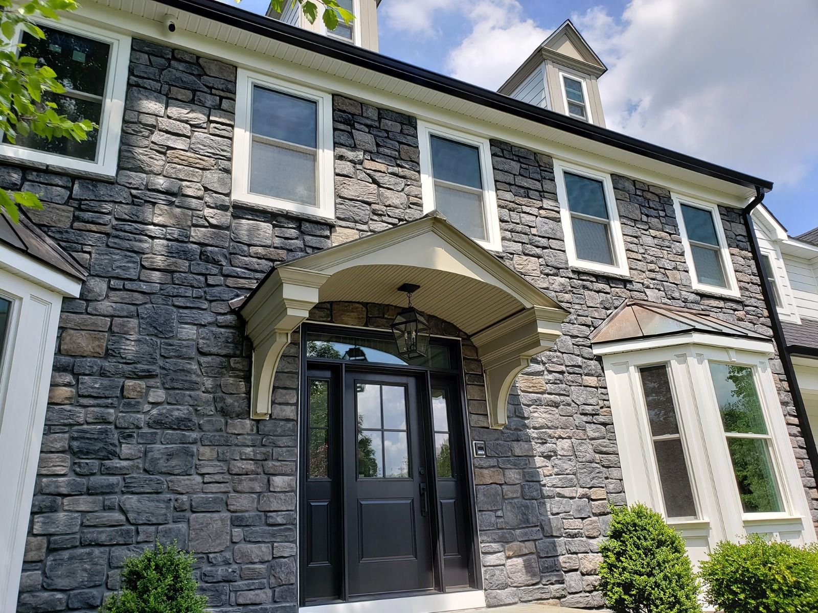 Stone facade of a house with many windows and a black front door under a beige portico.