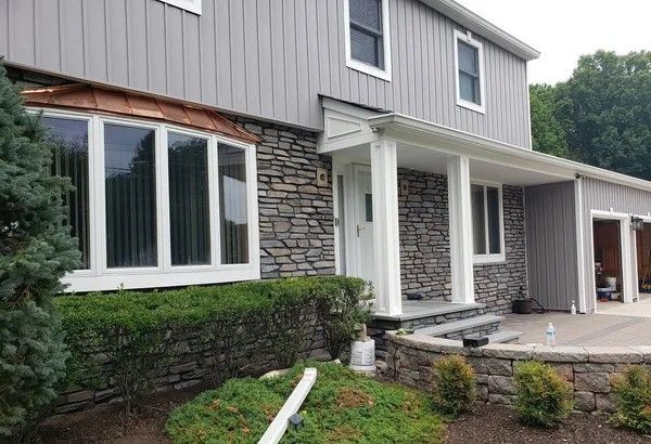 Gray house with stone facade, bay window, and white trim. Landscaping in front.