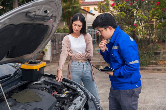 A man and a woman are looking under the hood of a car.