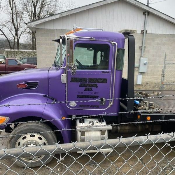 A purple tow truck is parked behind a chain link fence