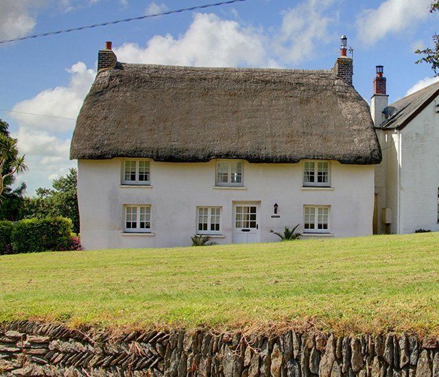 A white house with a thatched roof sits on top of a grassy hill