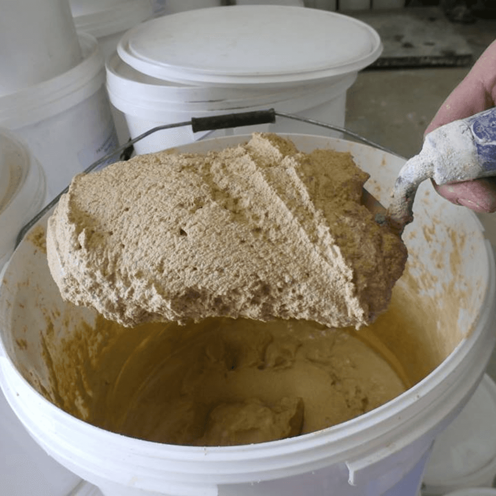 A person is mixing something in a bucket with a spatula