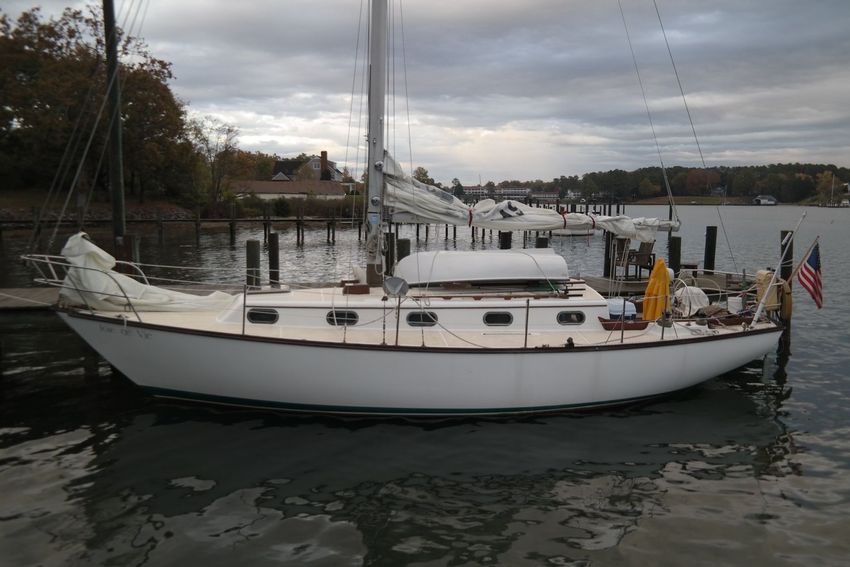A white sailboat docked at a pier on a cloudy day, with a US flag flying at the stern.