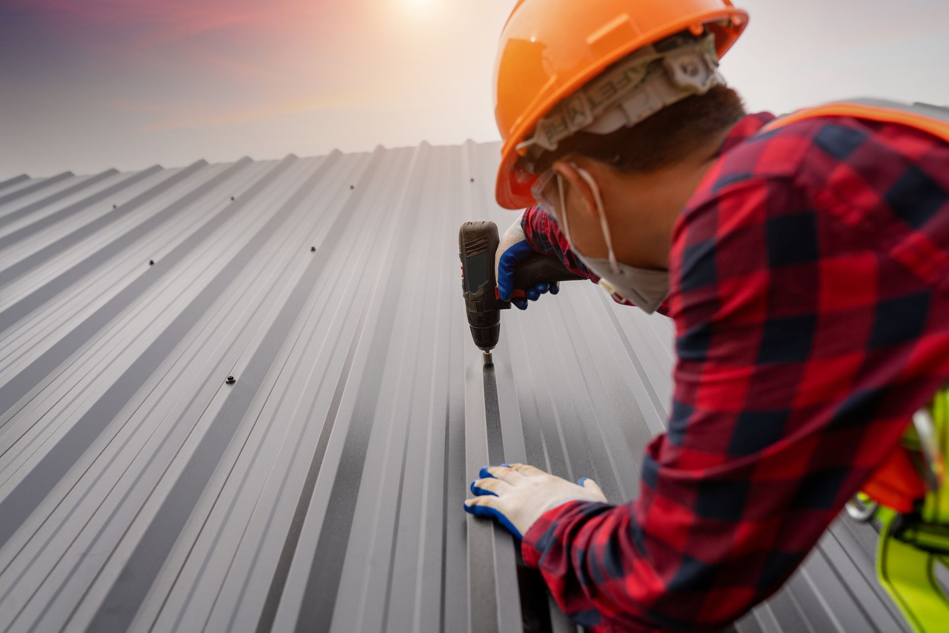 Commercial roofing contractor in safety gear installing a metal roof using a drill.
