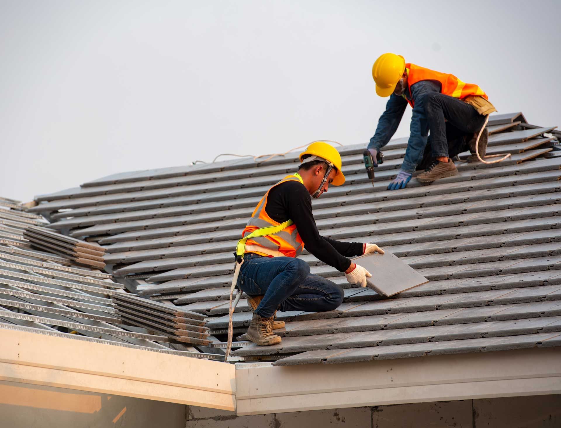 Roofing installation contractor fitting gray roof tiles on new house construction site.