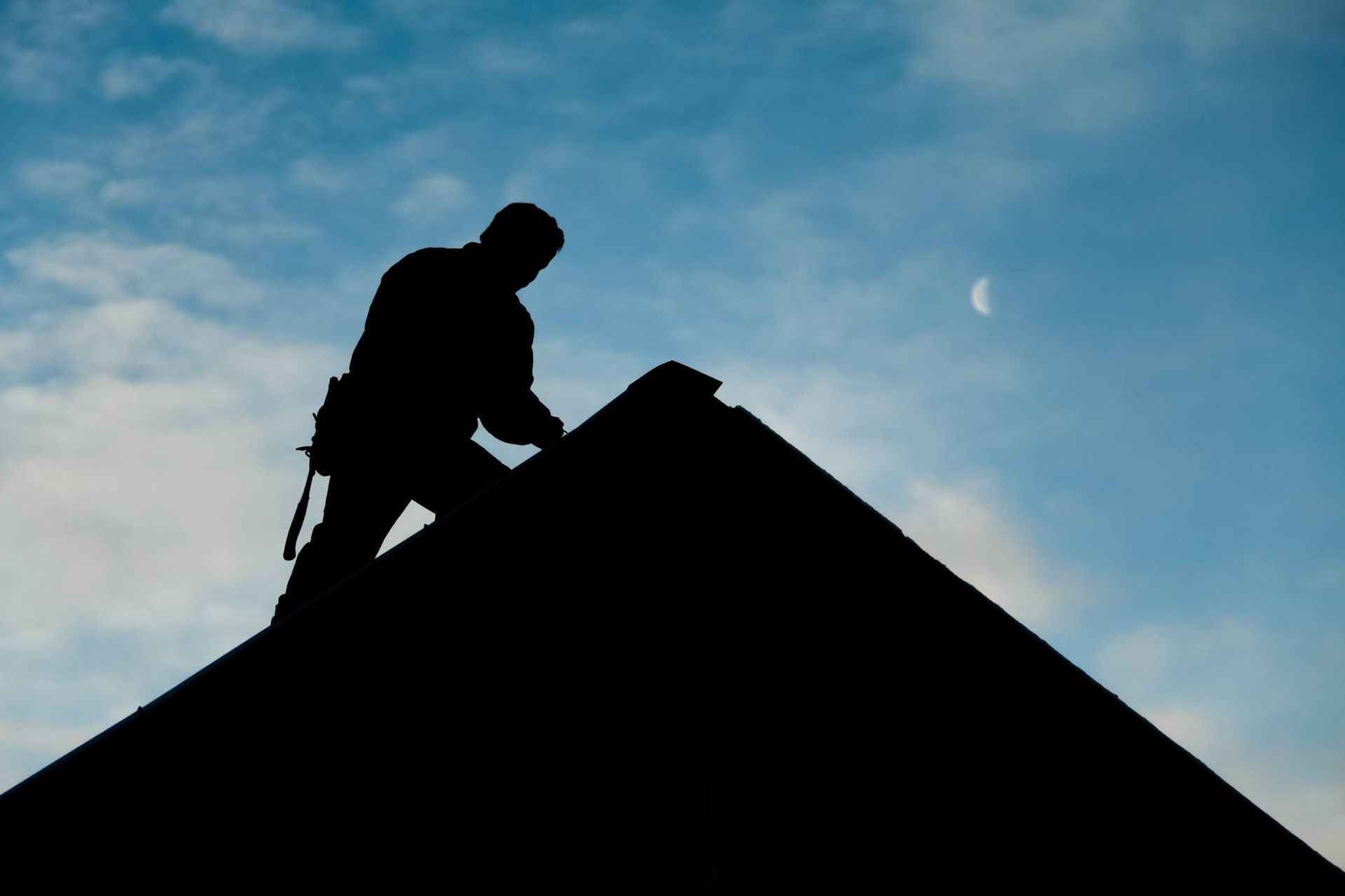 Roofer climbing on a roof near the ridge. Silhouette of a roofer inspecting a roof.