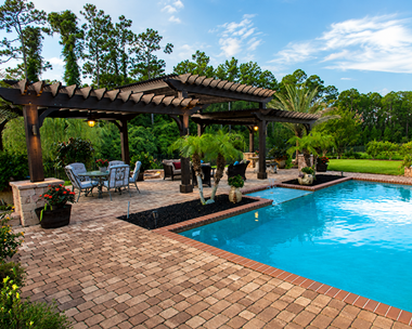 Patio pergola beside a bright blue swimming pool, with lounge chairs and lush green landscaping