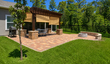 Backyard patio with pergola, stone fire pit, outdoor seating, and green lawn under bright sun