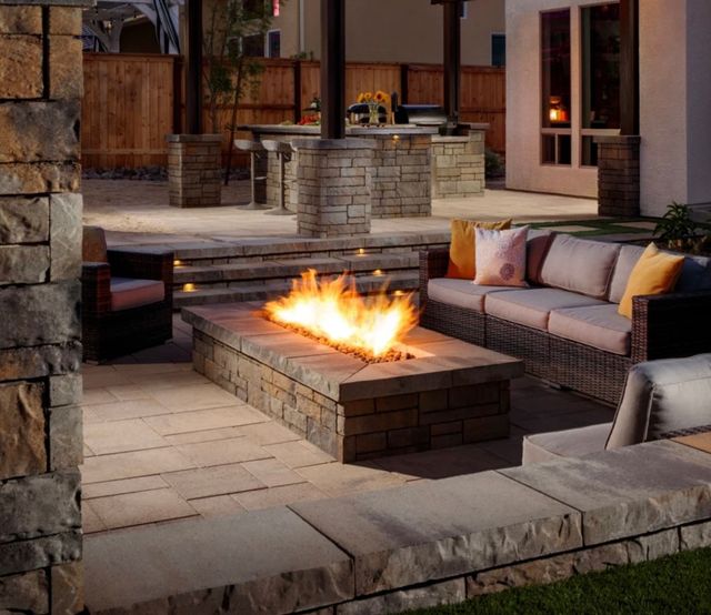 Outdoor patio with a stone fire pit, built-in seating, and cushioned sofas at dusk