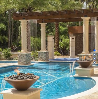 Resort pool with turquoise water, stone fire bowls, and a pergola surrounded by palm trees.