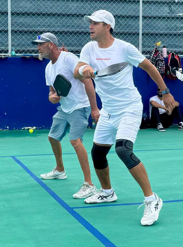 Two men are playing pickleball on a green court at the Playa Del Carmen Pickleball Club in Playa Del Carmen, Mexico