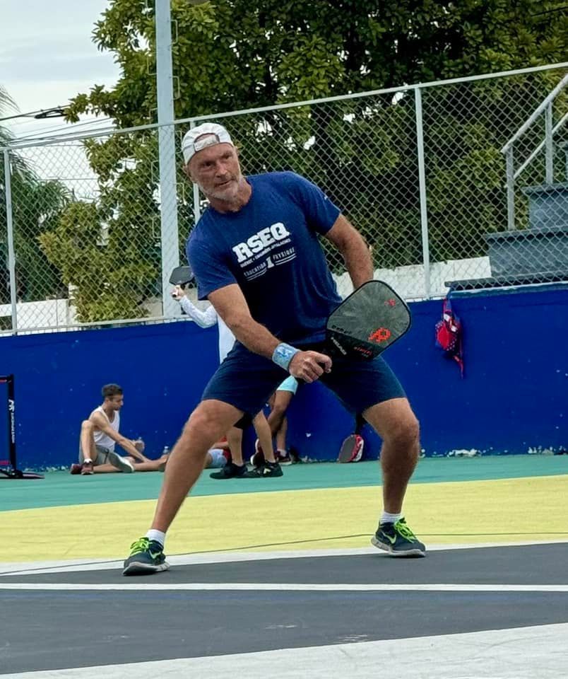 A man in a blue shirt that says rseq is playing pickleball
