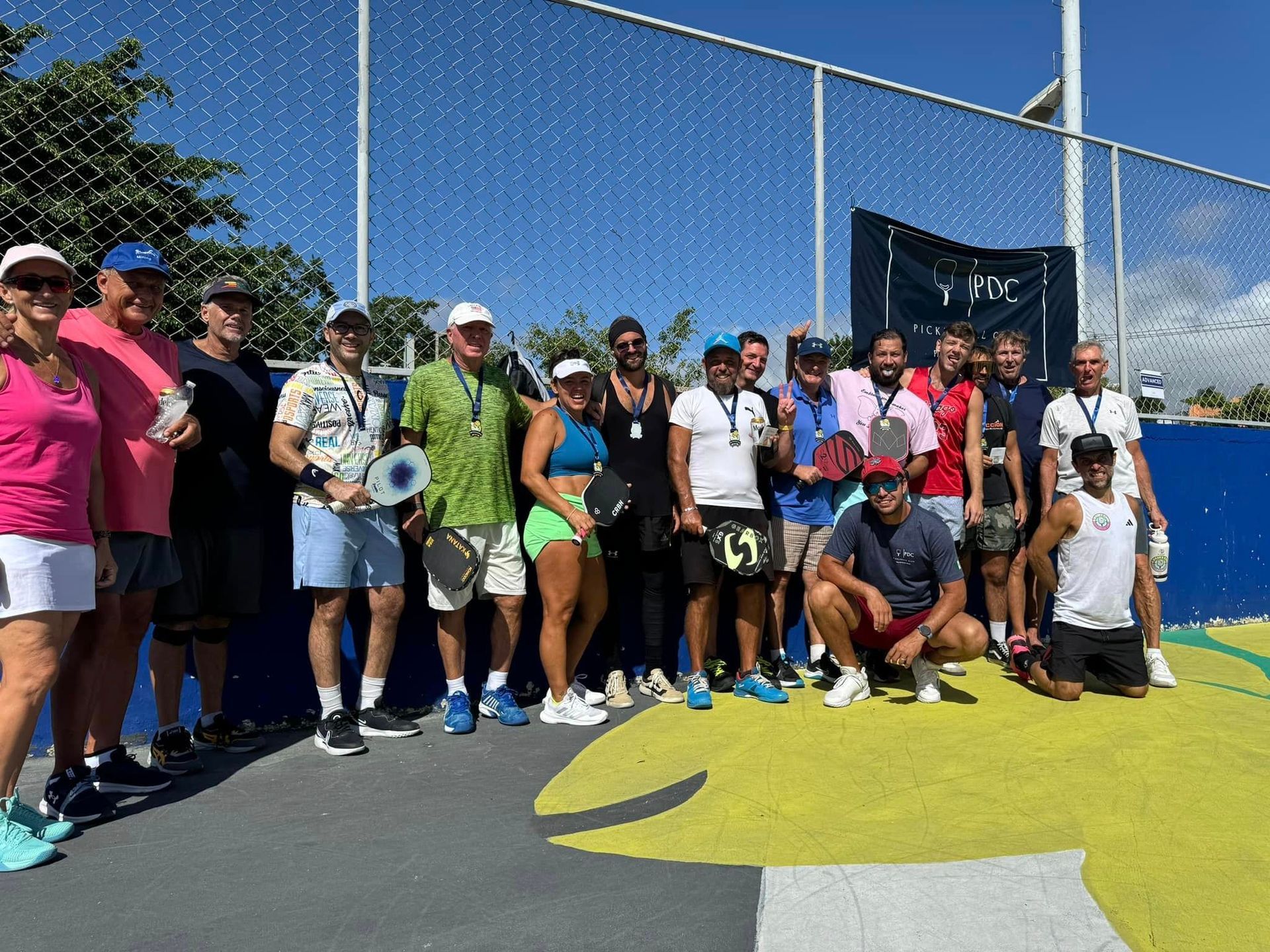 A group of people are posing for a picture on a pickleball court  at the Playa Del Carmen Pickleball Club in Playa Del Carmen, Mexico