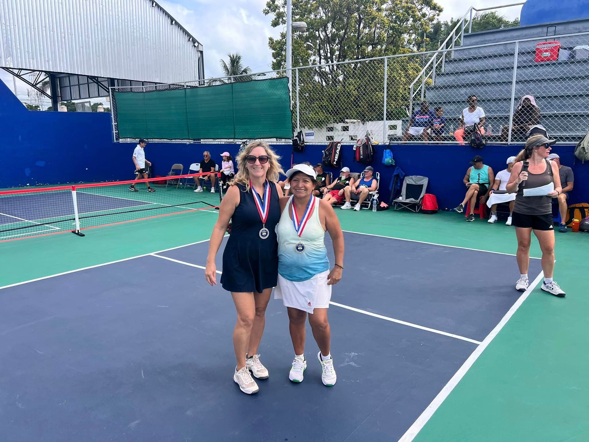 Two women are posing for a picture on a pickleball court.   at the Playa Del Carmen Pickleball Club in Playa Del Carmen, Mexico rackets.