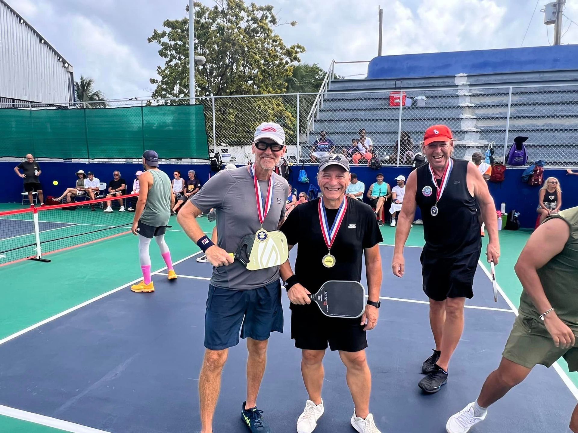 A group of men are posing for a picture on a pickleball court  at the Playa Del Carmen Pickleball Club in Playa Del Carmen, Mexico rackets.