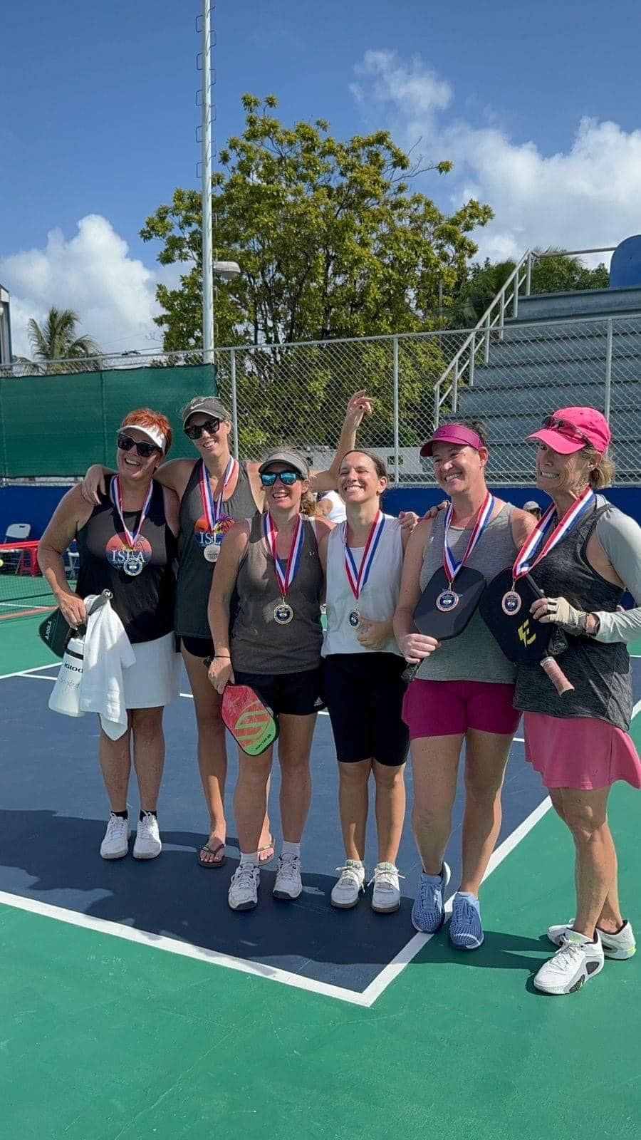 A group of women are posing for a picture on a pickleball court.  at the Playa Del Carmen Pickleball Club in Playa Del Carmen, Mexico rackets.