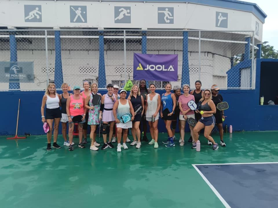 A group of pickleball players are posing for a picture on a pickleball court at the Playa Del Carmen Pickleball Club in Playa Del Carmen, Mexico rackets.