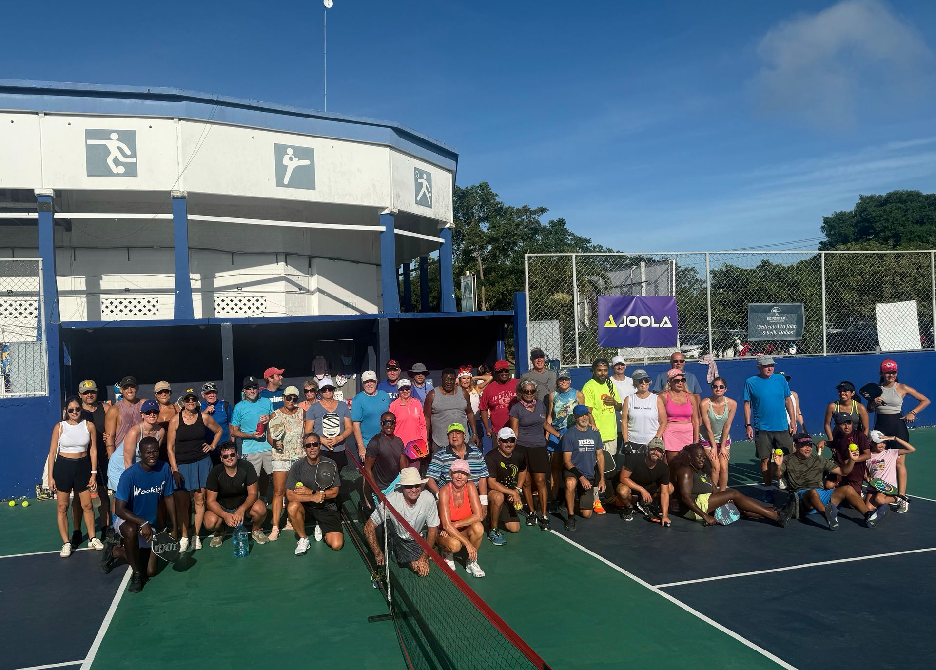 A group of people posing for a picture on a pickleball court at the Playa Del Carmen Pickleball Club in Playa Del Carmen, Mexico rackets.