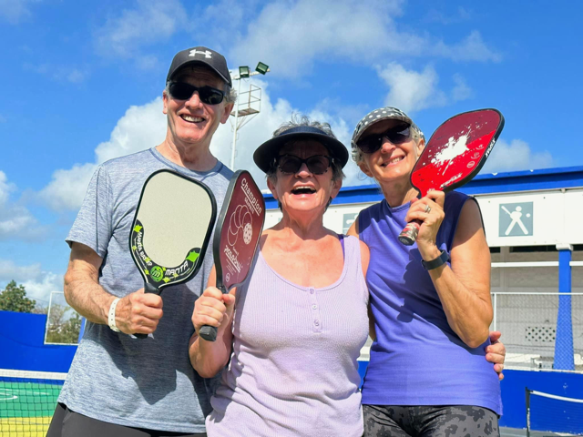 A man and two women are holding paddle rackets on a pickleball court.