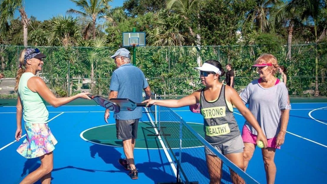 A group of people are shaking hands on a pickleball court at the Playa Del Carmen Pickleball Club in Playa Del Carmen, Mexico