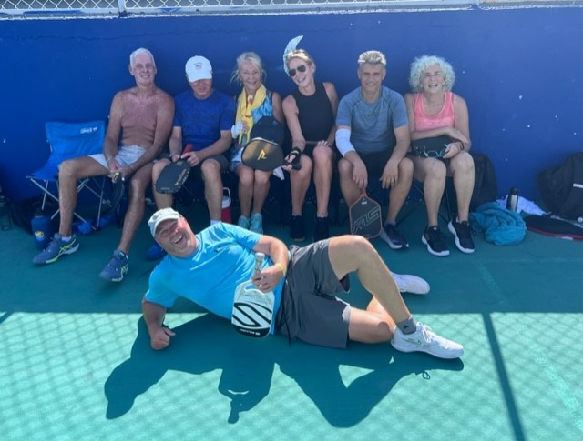 A group of PDC pickleball club members are posing for a picture on a pickleball court  at the Playa Del Carmen Pickleball Club in Playa Del Carmen, Mexico