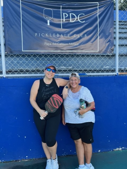 Two women are posing for a picture in front of a pdc pickleball sign