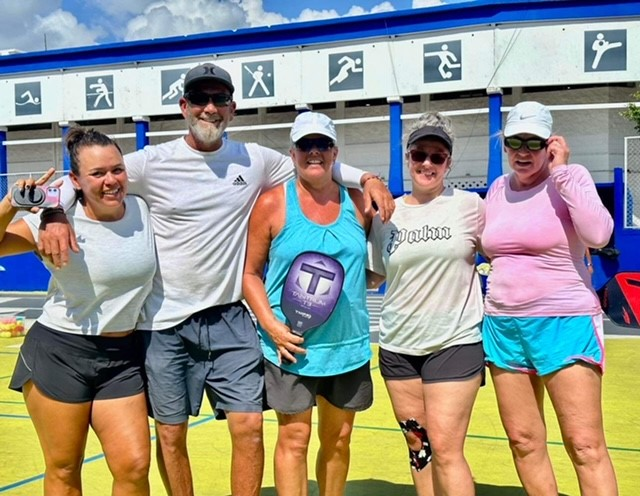 A group of people are posing for a picture on a pickleball court.