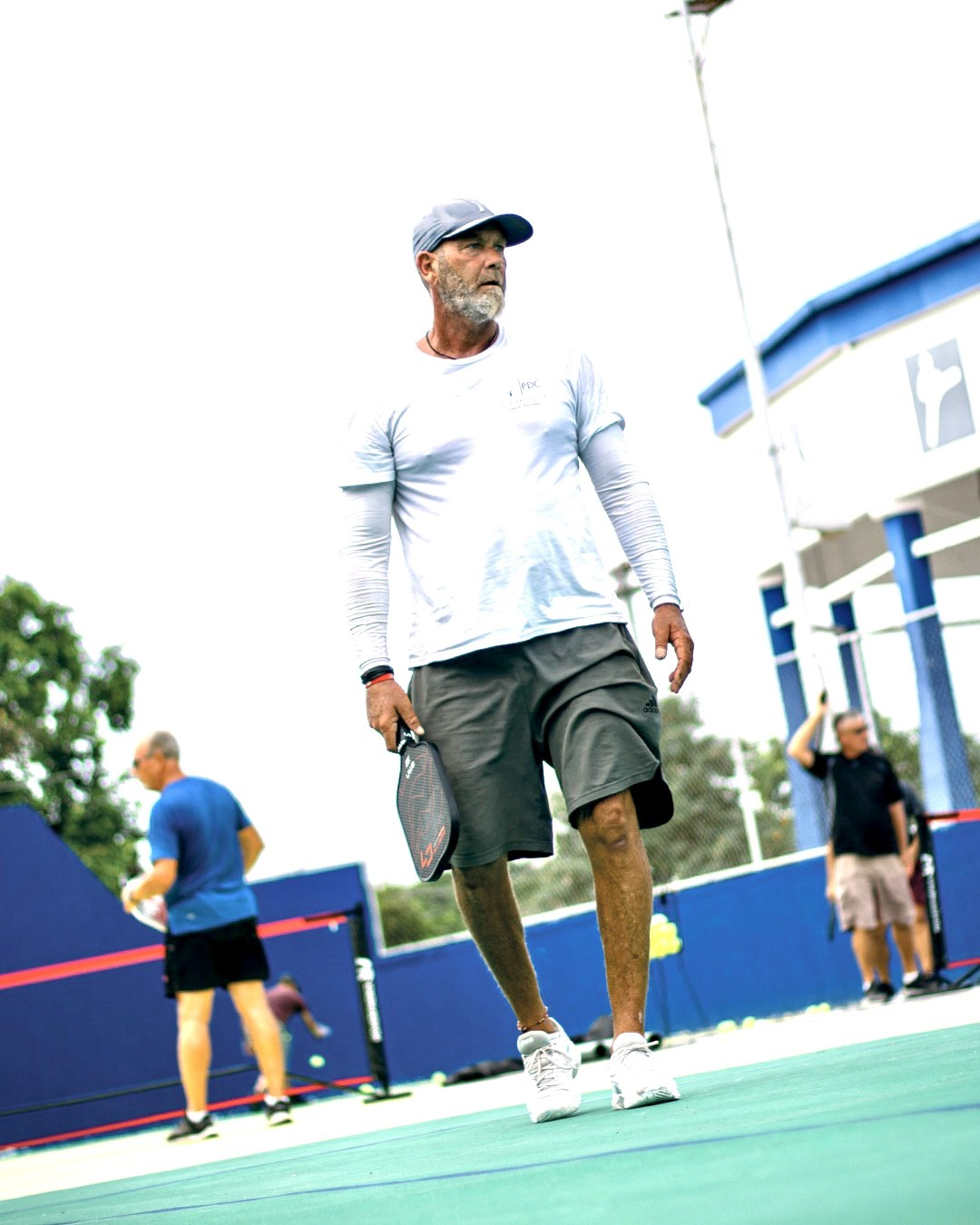 A man is walking on a tennis court holding a pickleballracket.