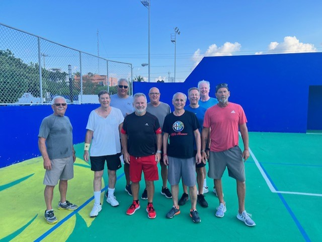 A group of men are posing for a picture on a pickleball court