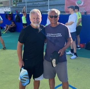 Two men are posing for a picture on a pickleball court