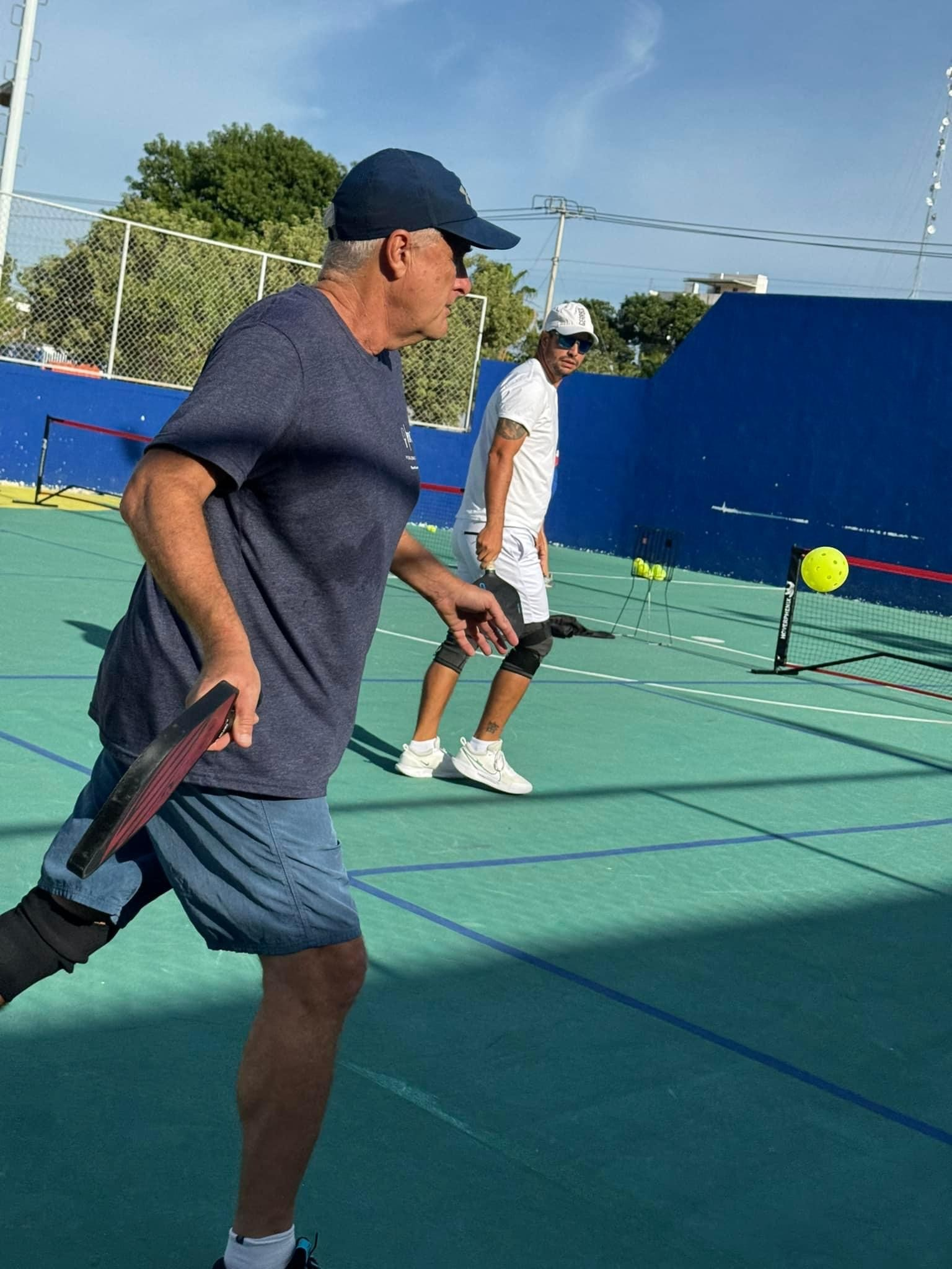 Two men are playing tpickleball on a green court.