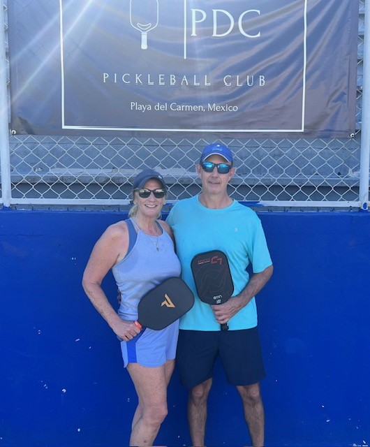 A man and a woman standing in front of a pickleball club banner