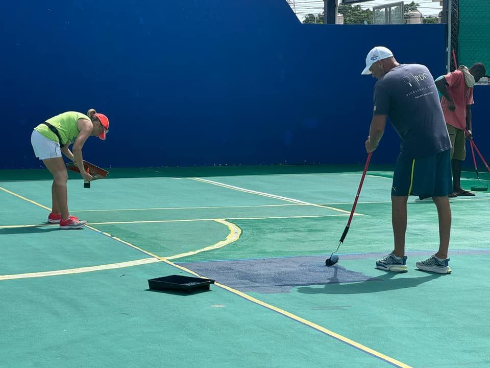 A group of people are painting the pickleball court  at the Playa Del Carmen Pickleball Club in Playa Del Carmen, Mexico rackets.