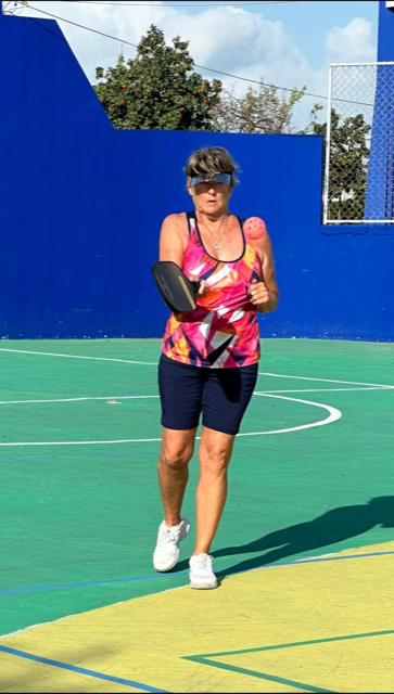 A woman is running on a pickleball court with a blue wall in the background  at the Playa Del Carmen Pickleball Club in Playa Del Carmen, Mexico