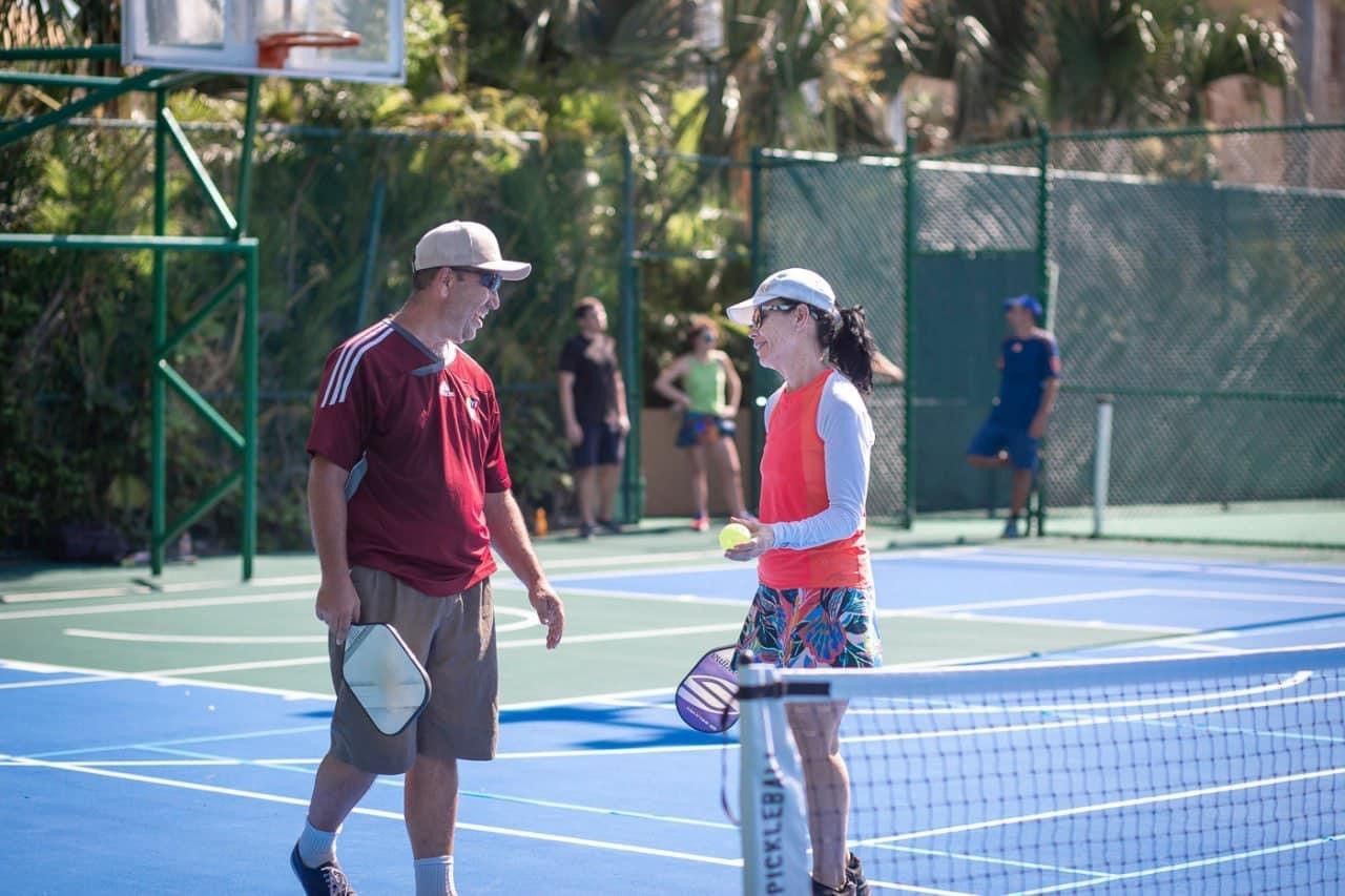 A man and a woman are talking on a pickleballcourt.