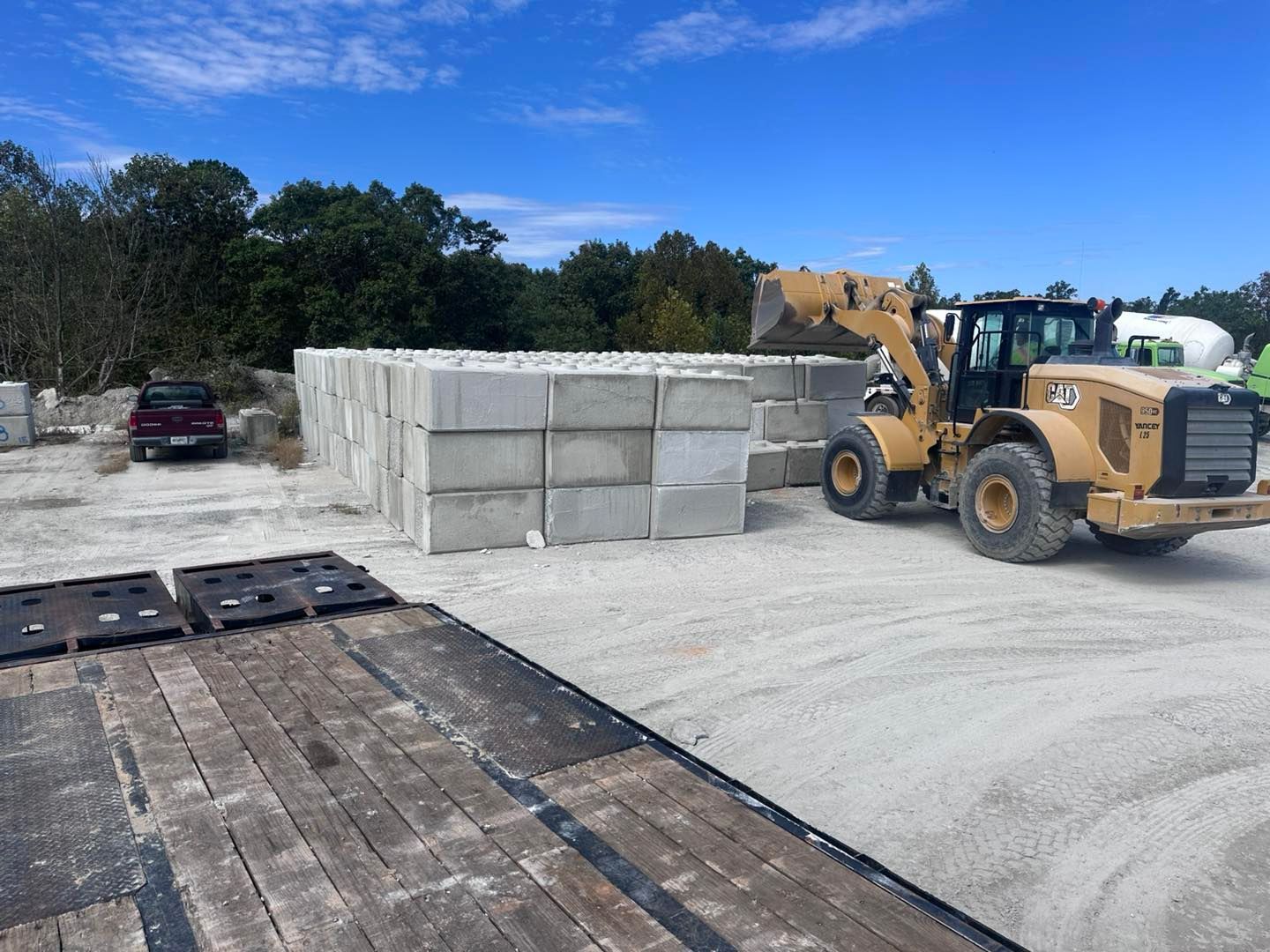 Yellow loader moving concrete blocks in a gravel yard under a blue sky.