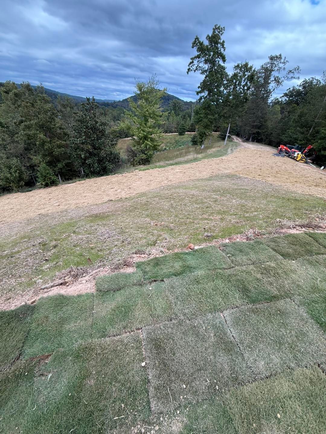 Grassy hillside with sod installation, under cloudy skies.