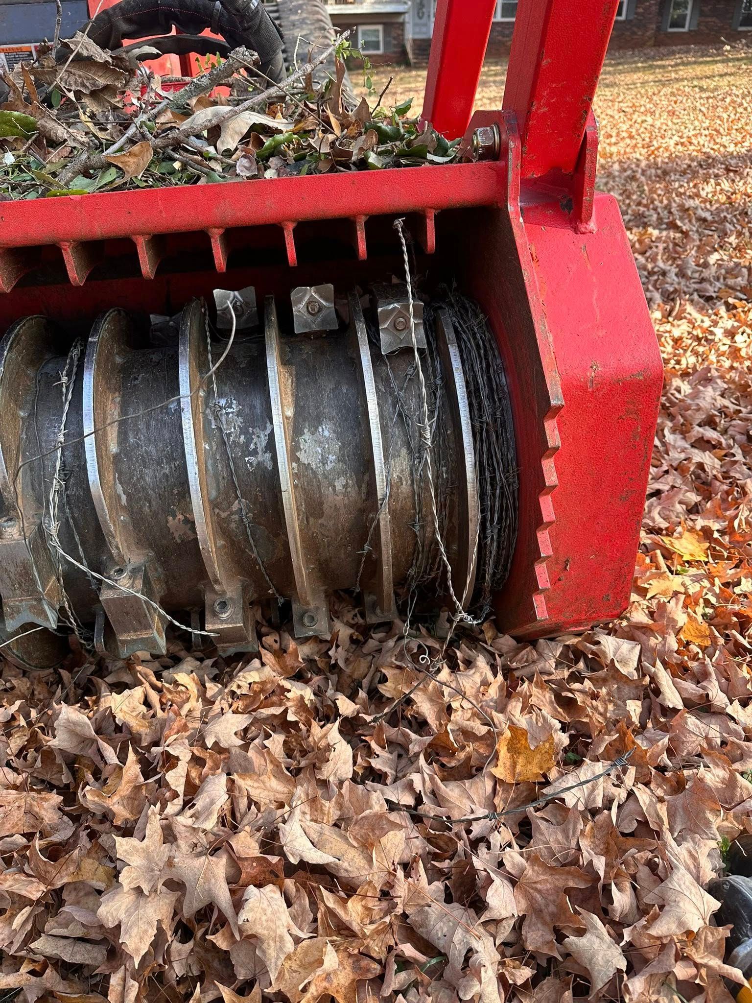 Red industrial grapple scooping up leaves on the ground.