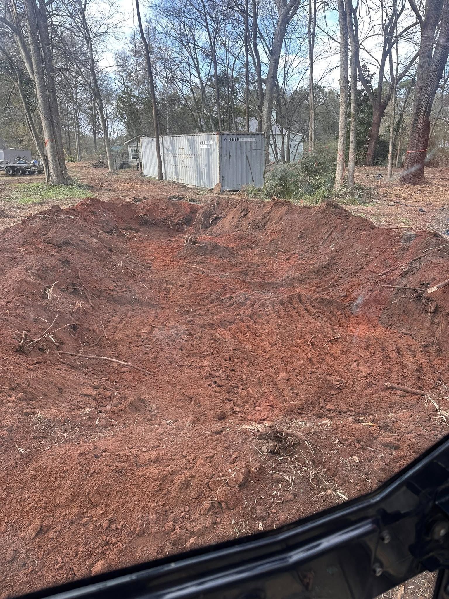 A pile of red mulch in a forest clearing, with a concrete structure in the background.